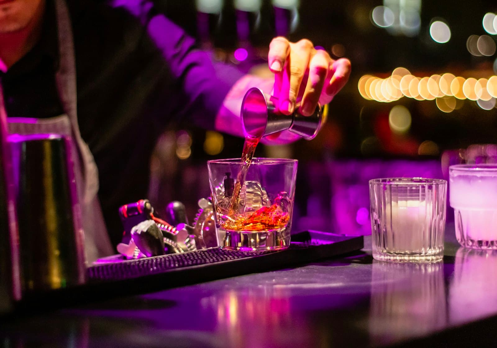 A bartender pouring a drink under purple light